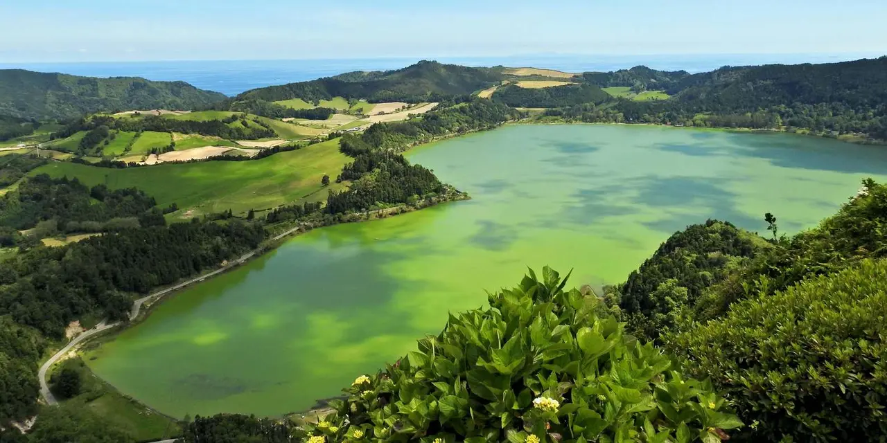 Furnas lake's green water filling a wooded volcanic valley, the sea on the horizon