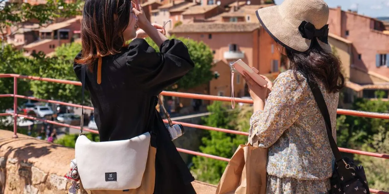 Two visitors in sun hats looking out over a hill village of ochre-coloured houses