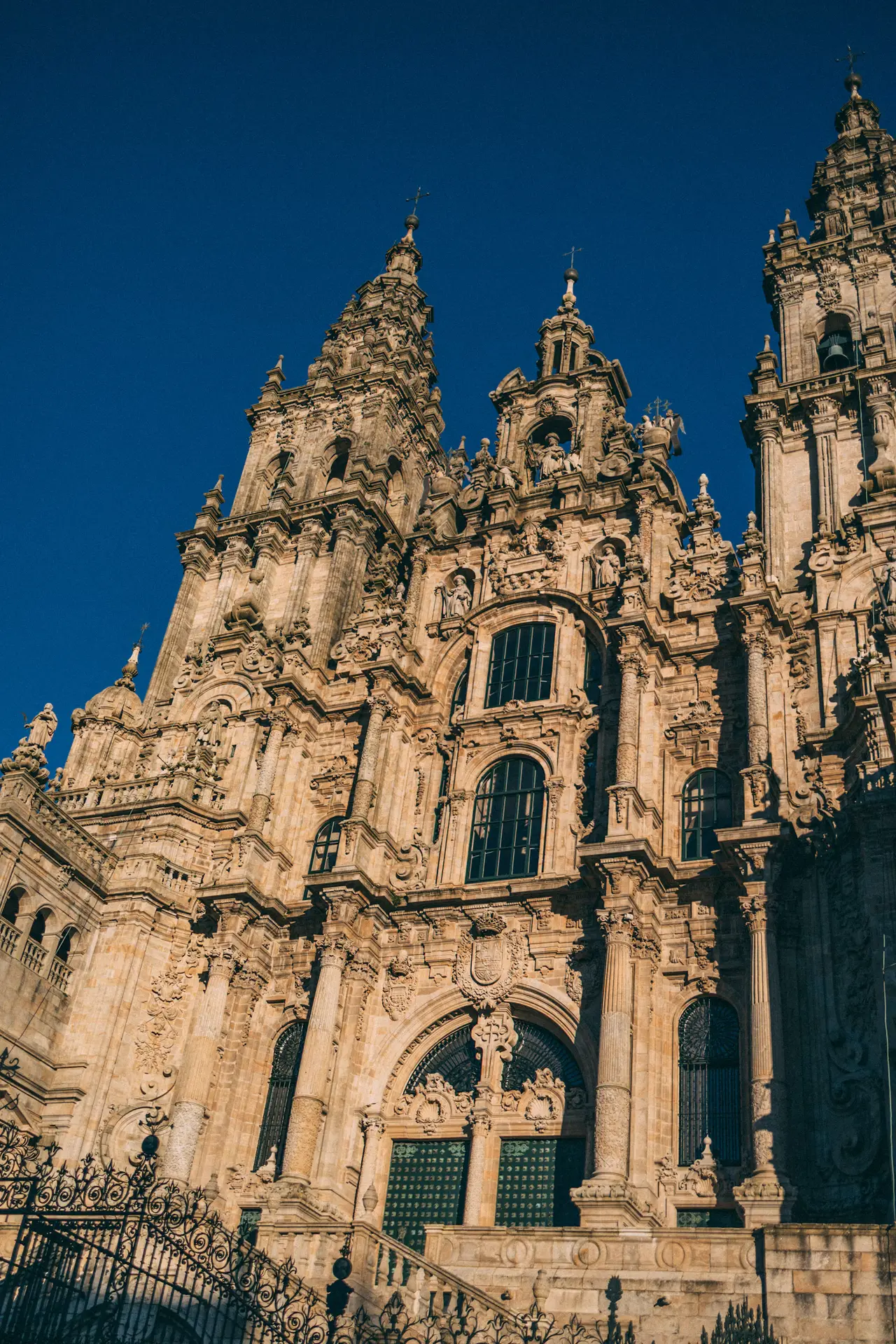 The ornate baroque façade and towers of Santiago de Compostela cathedral on Praza do Obradoiro, against a deep blue sky