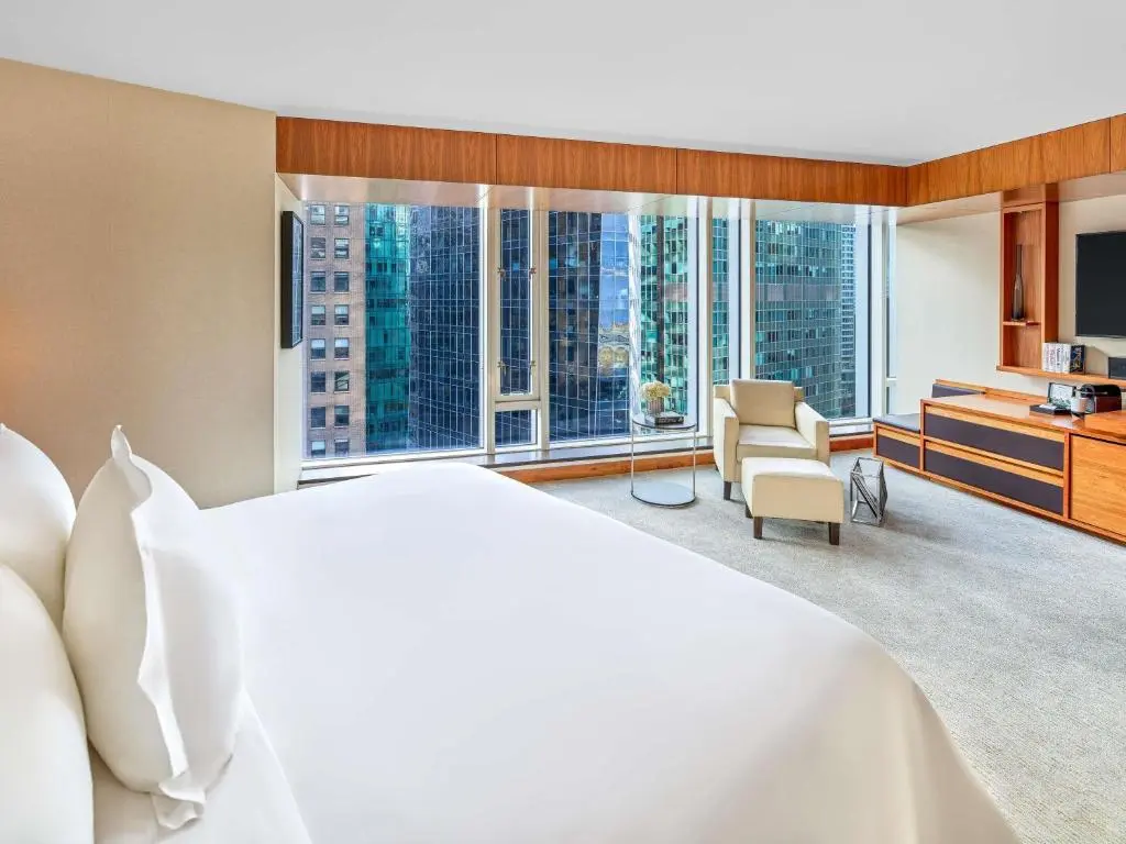 A Fairmont Pacific Rim guest room with a white bed and floor-to-ceiling windows onto downtown Vancouver's glass towers