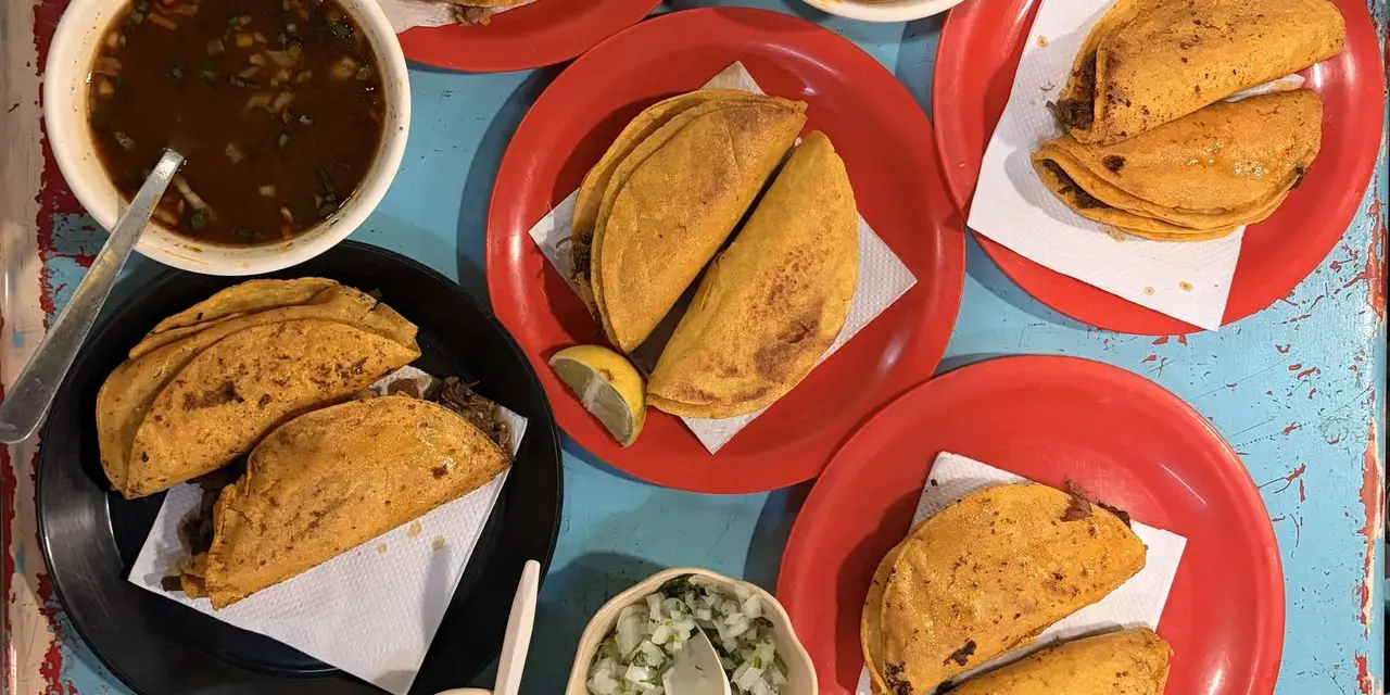 Fried empanadas on red plates with small bowls of soup on a blue table