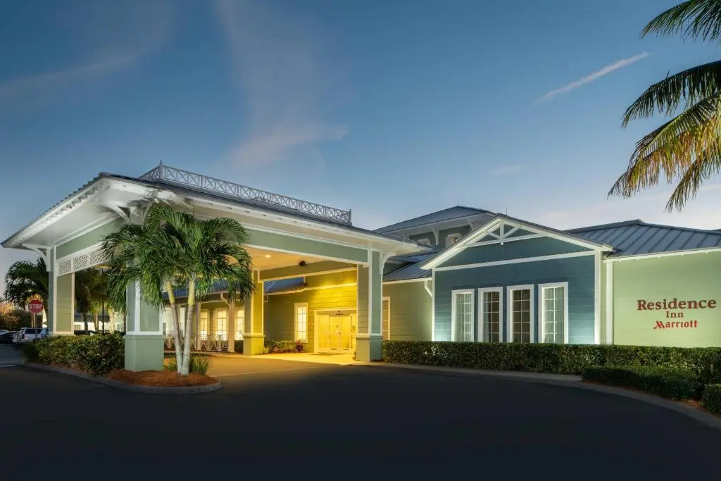 The Residence Inn entrance at dusk, a lit covered porte-cochère with palm trees and green and blue Florida-style cladding and the Residence Inn Marriott sign
