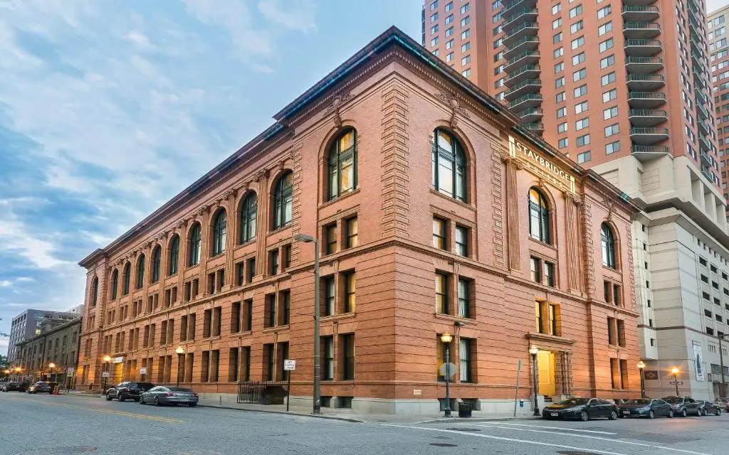 The red-brick, arched-window corner of the Staybridge Suites Baltimore Inner Harbor, a restored 1904 building, seen from the street at dusk
