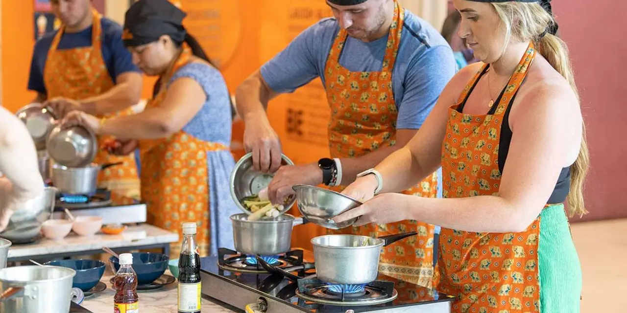 Cooks in aprons working at gas burners in an orange-walled kitchen