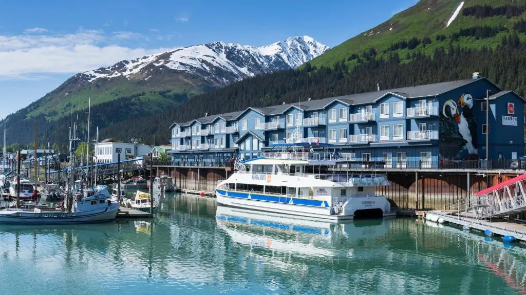 Harbor 360 Hotel's blue three-storey building on the Seward Small Boat Harbor, with a tour boat at its dock and snow-streaked mountains behind