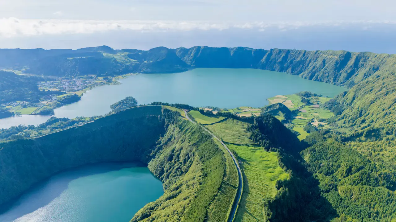 Aerial view of two crater lakes on São Miguel, a large blue lake inside a green volcanic caldera and a smaller one in the foreground crater, a road running along the ridge between them