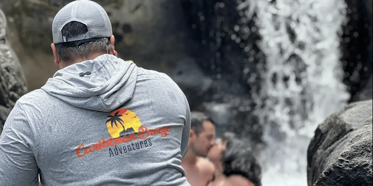 A guide in a grey hooded top watching swimmers near a rainforest waterfall