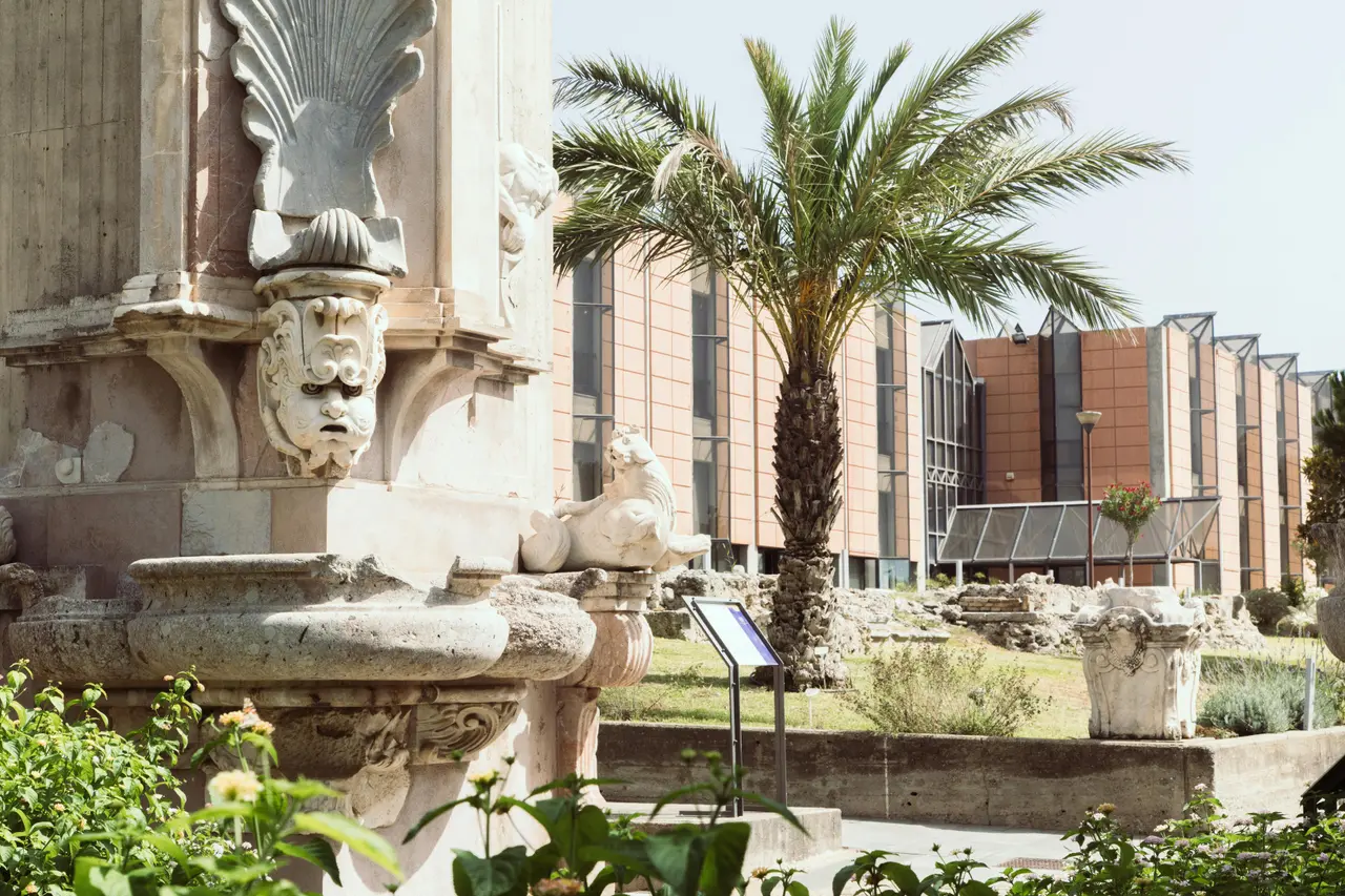 A carved stone fountain and a palm tree in the museum garden, with the modern museum building behind
