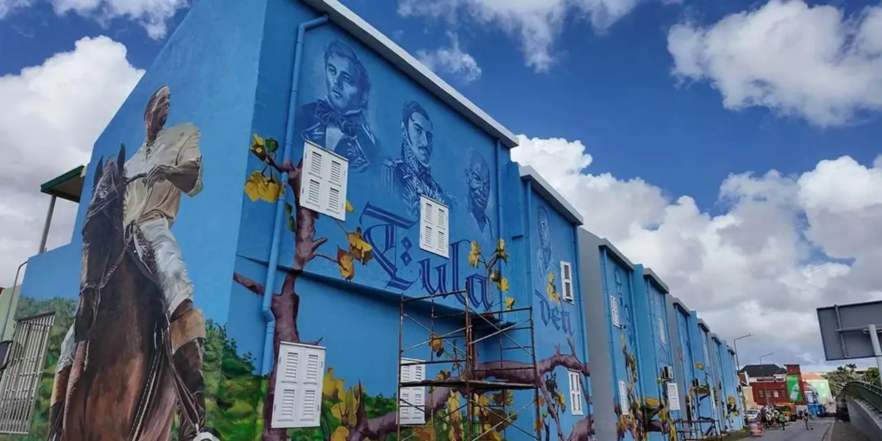 A long blue building painted with large murals of historical figures under a cloudy sky