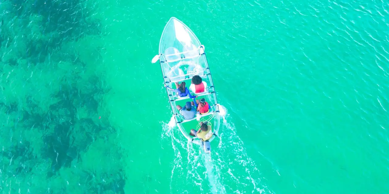 Aerial view of a small clear-hulled boat carrying several people across bright turquoise water