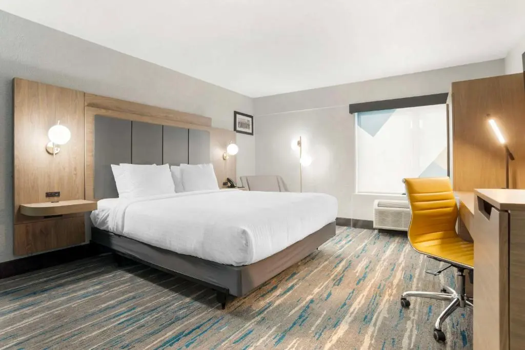A Best Western Plus room with a white king bed, wood headboard and a yellow desk chair