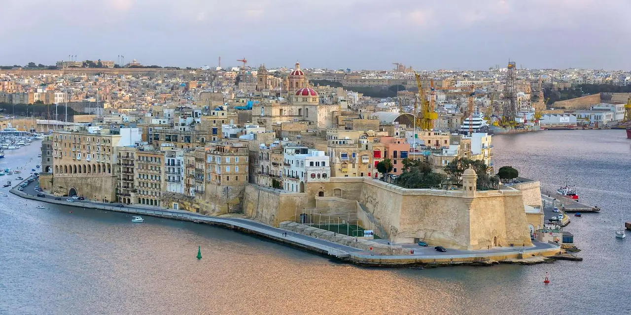 A fortress on a point in the deep blue Grand Harbour, with a small boat passing in front