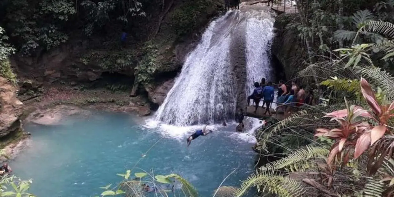 A waterfall dropping into a turquoise pool in the forest with a swimmer below