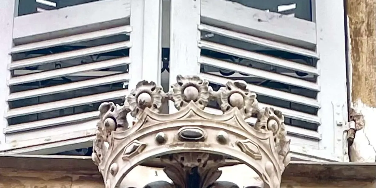 A carved stone coat of arms with a crown below a shuttered window