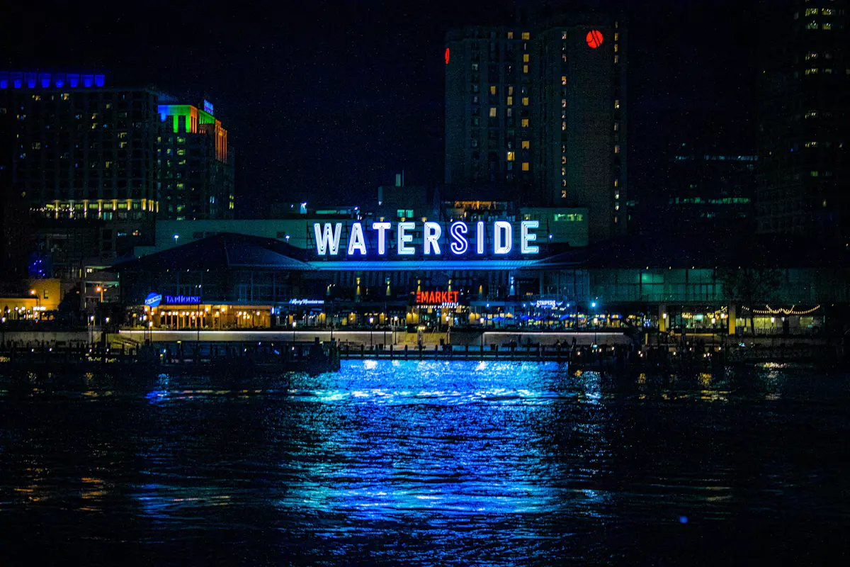 The glowing blue Waterside sign over Norfolk's downtown waterfront at night, reflected in the dark water of the Elizabeth River