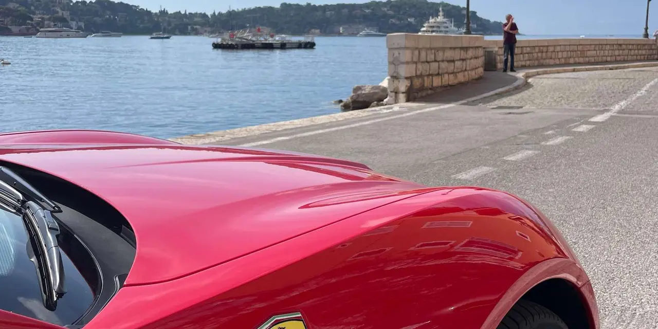 A red Ferrari parked on the Villefranche waterfront with the bay behind