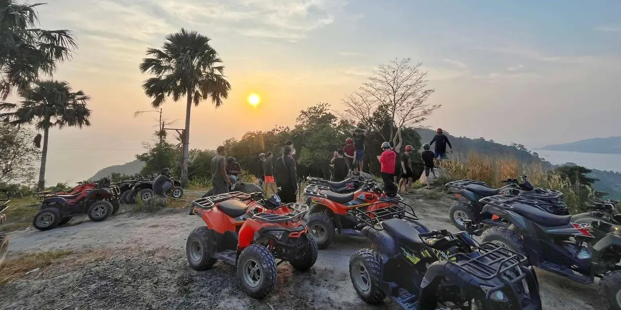 ATVs parked on a hilltop at sunset, with palm trees against an orange sky