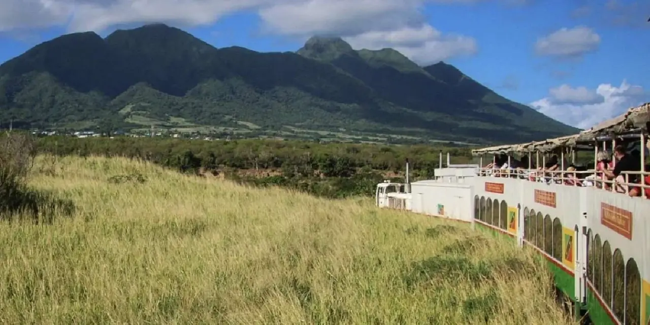 A double-deck tour train on a grassy hillside with the island's green volcanic ridge behind it