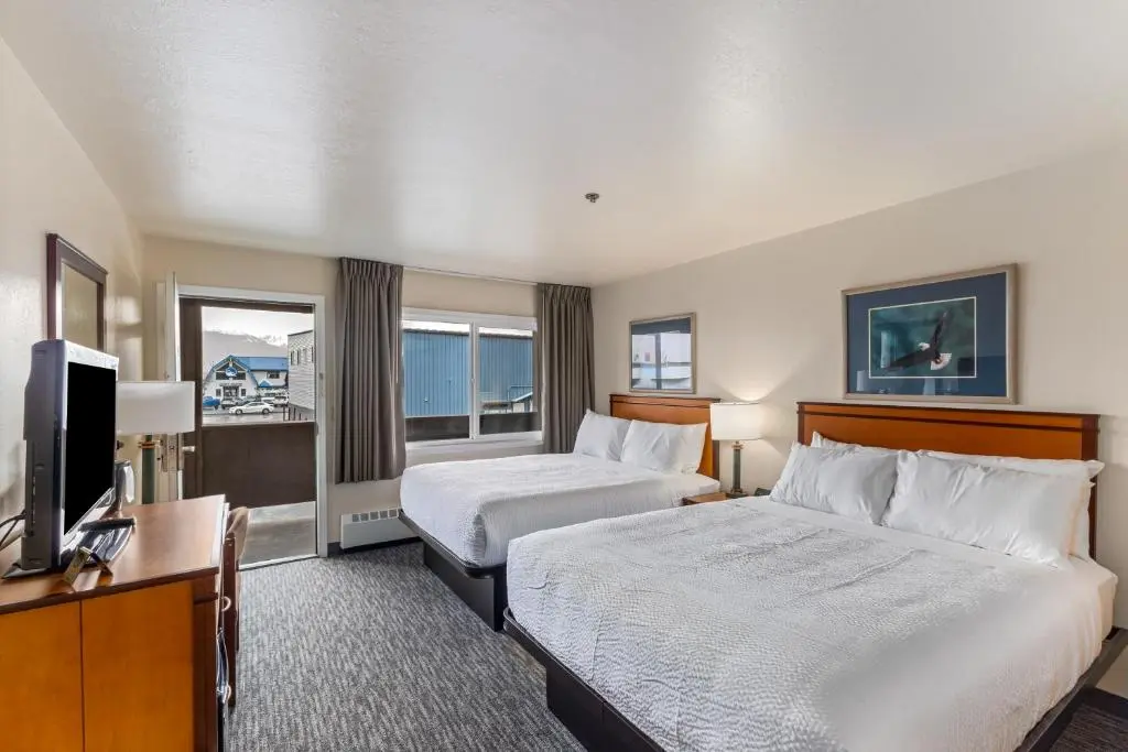 A Breeze Inn guest room with two queen beds, a flat-screen TV and a door to a small balcony looking toward the harbor