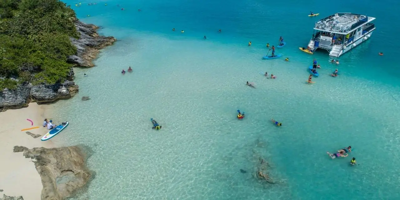 Aerial view of a pale-sand cove with kayaks on shallow turquoise water beside a green headland