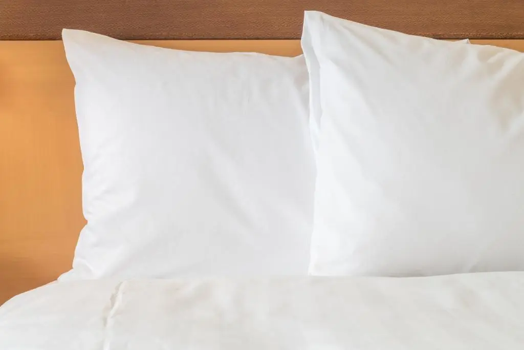 Two white pillows on a made bed against a wooden headboard at the Holiday Inn Mobile West I-10
