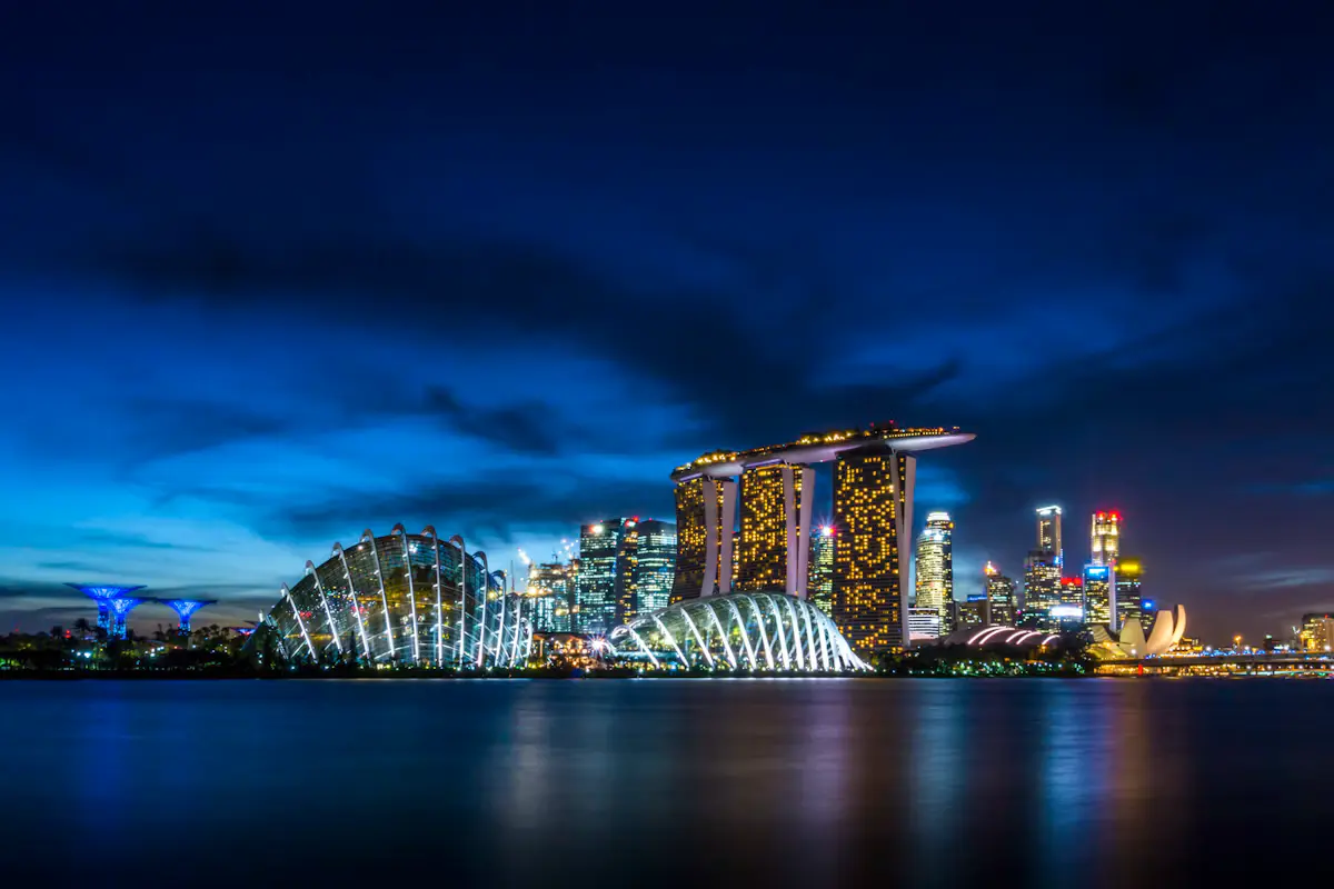 Marina Bay at blue hour: the lit Gardens by the Bay domes and Supertrees, Marina Bay Sands and the city towers reflected in the water