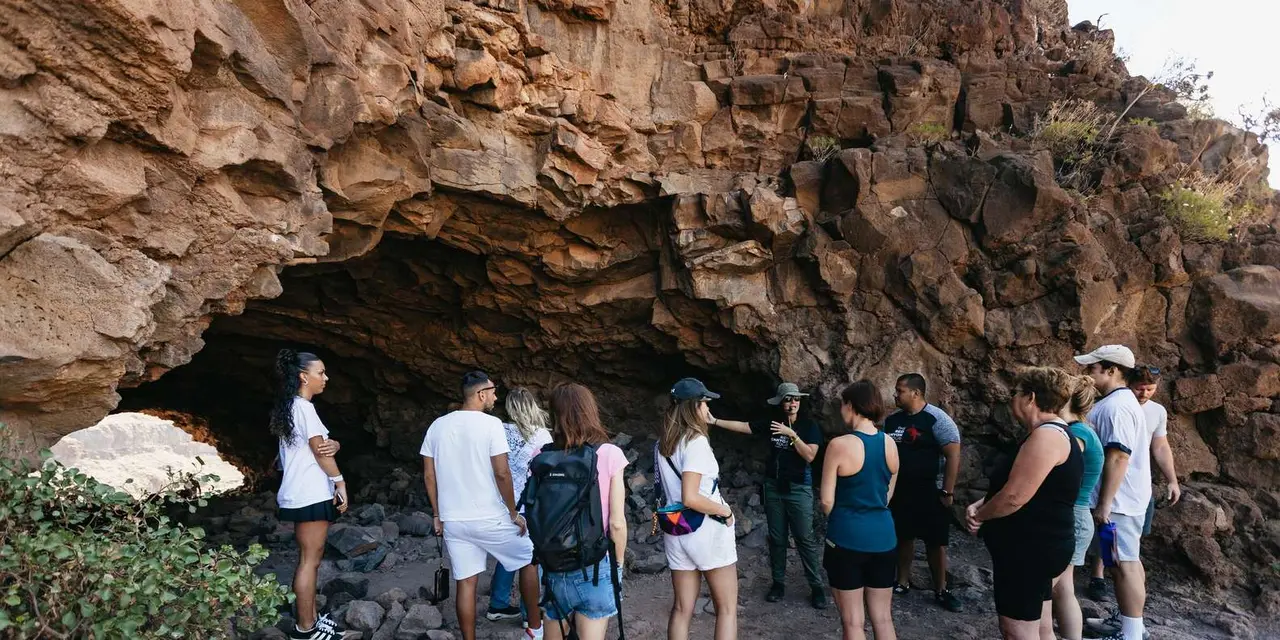 A guide talking to a group at the mouth of a red rock cave