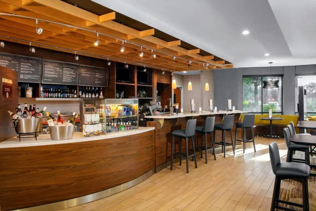 The Courtyard Jacksonville I-295 lobby bistro, a curved wood bar with bar stools and menu boards under a slatted timber ceiling