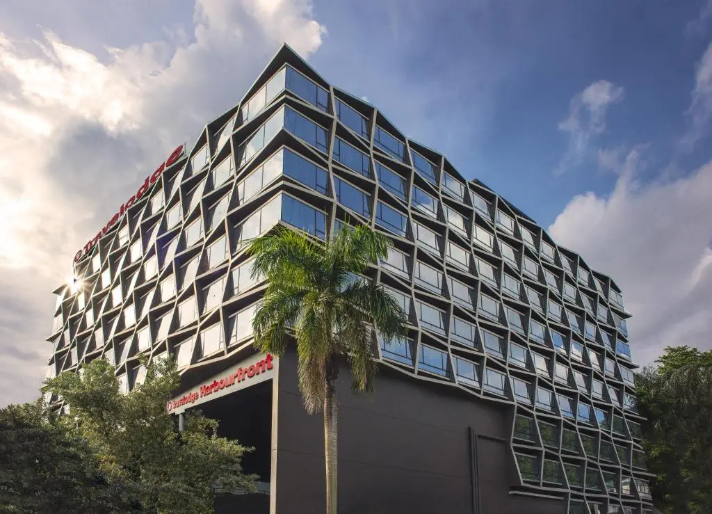 Travelodge Harbourfront's faceted glass facade rising above a palm tree, with the Travelodge Harbourfront sign over the entrance