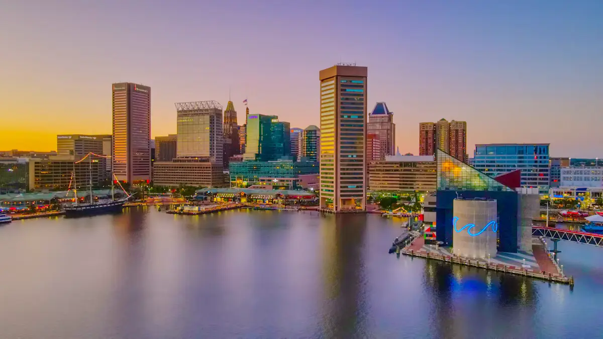 The Baltimore Inner Harbor skyline at sunset, with the World Trade Center tower, the glass-fronted National Aquarium and a tall ship across calm water