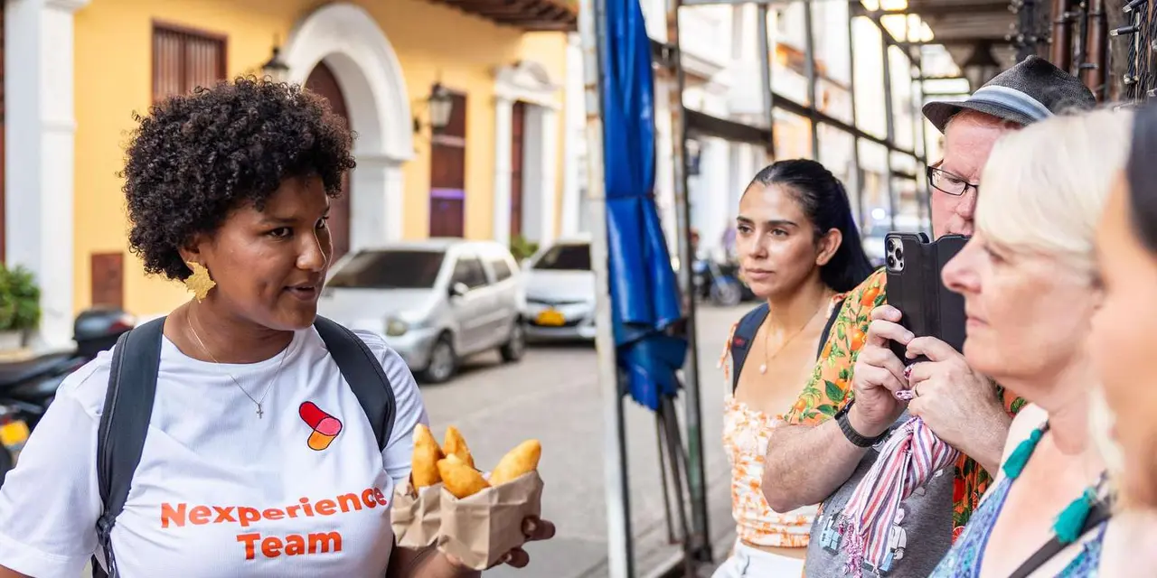 A smiling guide in a white T-shirt holding a paper tray of fried snacks on a city street
