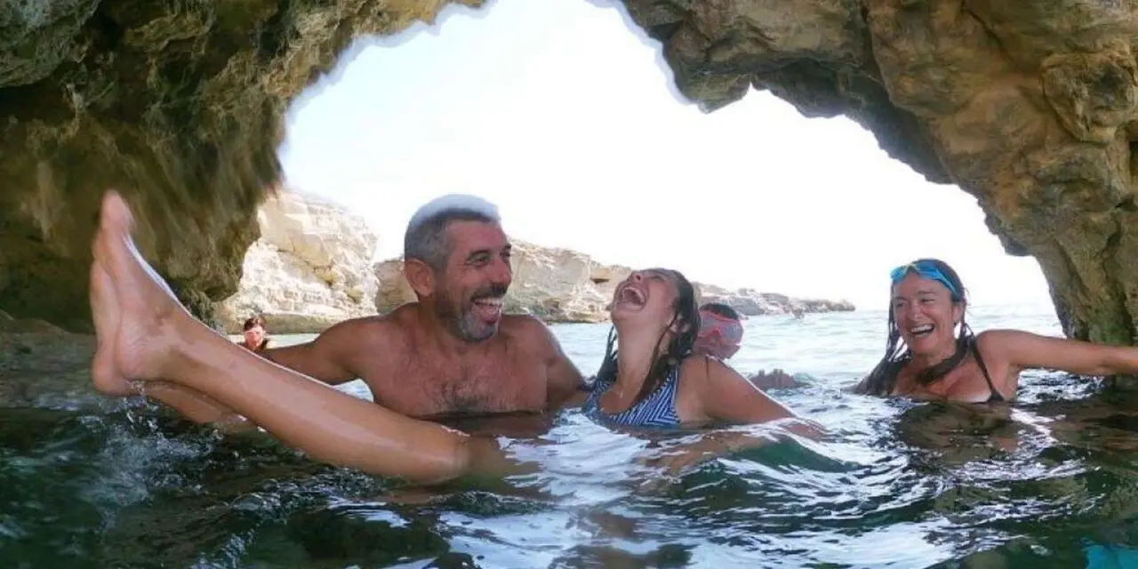 Three swimmers laughing in the water just inside the mouth of a rocky sea cave