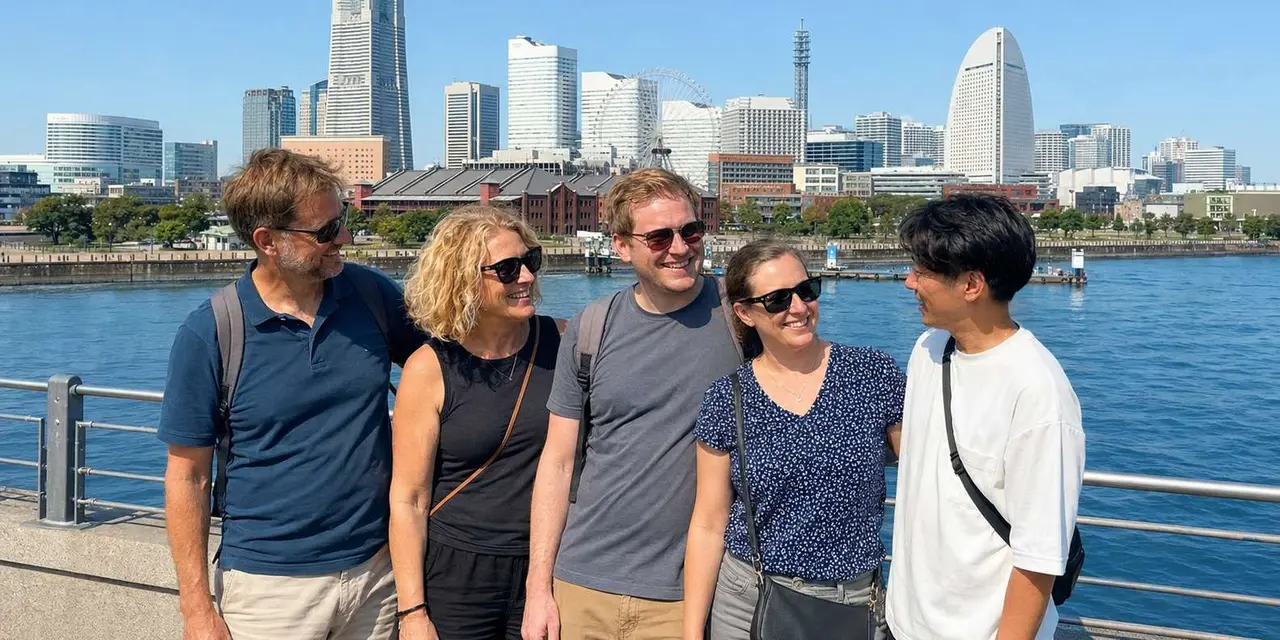 Five smiling visitors in sunglasses posing on a railing with Yokohama's Minato Mirai skyline and the Cosmo Clock 21 ferris wheel behind them