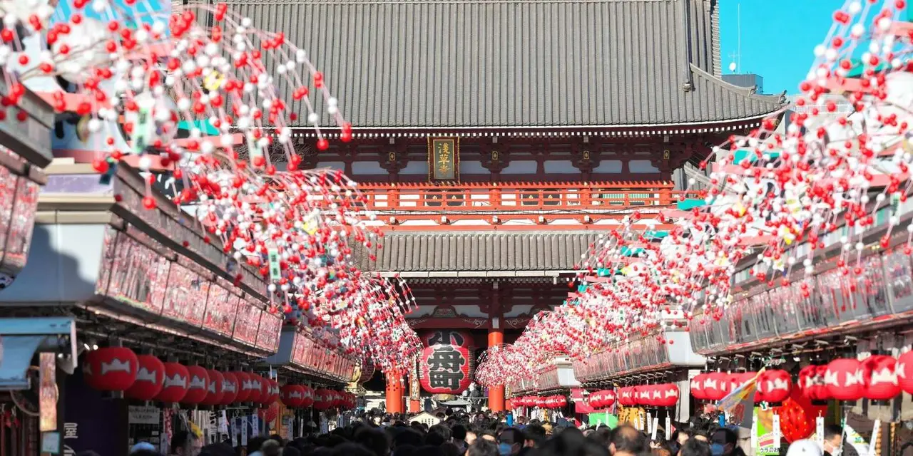 Crowds under a canopy of red and white ornaments on Nakamise Street, with the Hozomon gate and its giant red lantern ahead