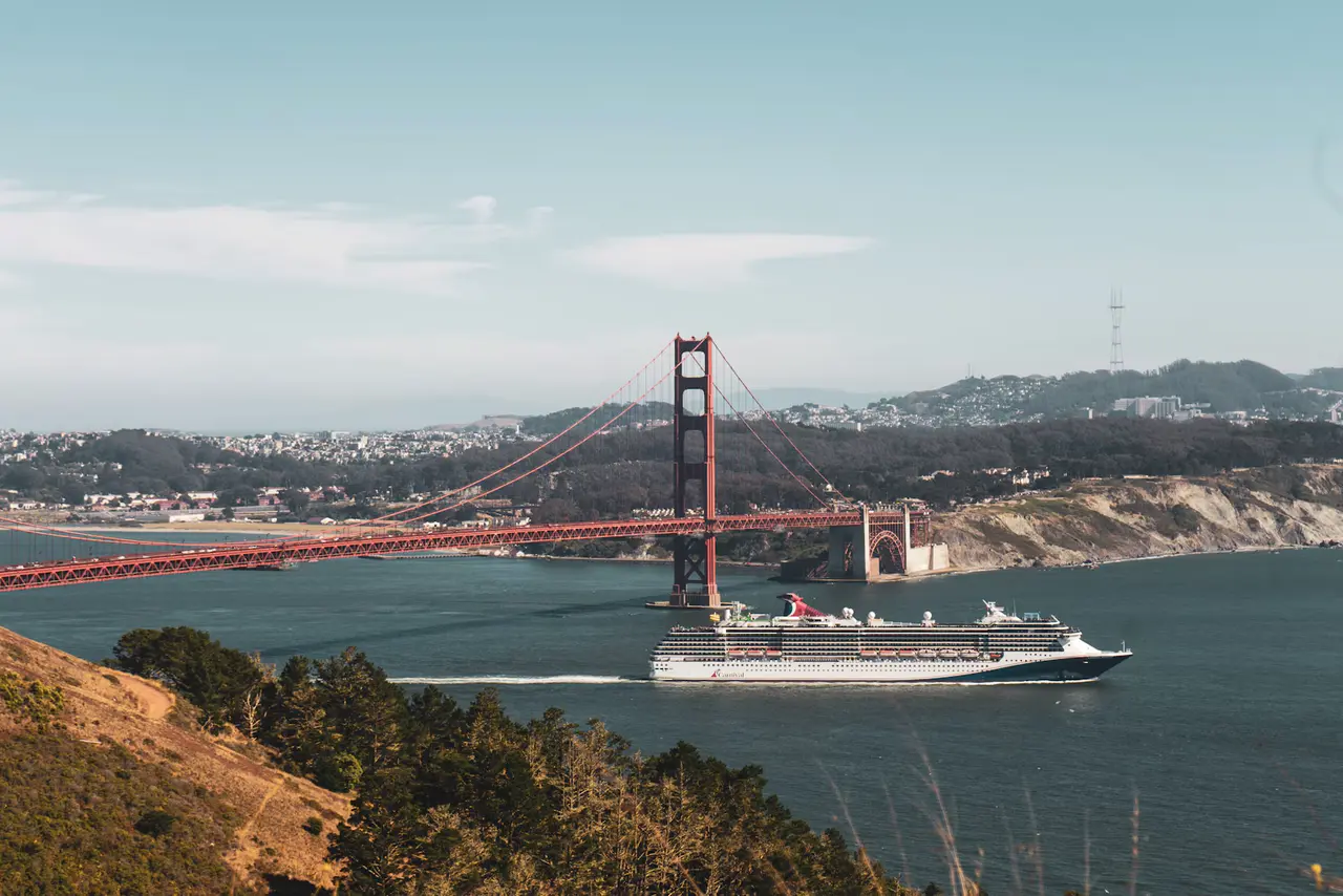 A cruise ship sailing out under the Golden Gate Bridge, seen from the green Marin Headlands on a clear day