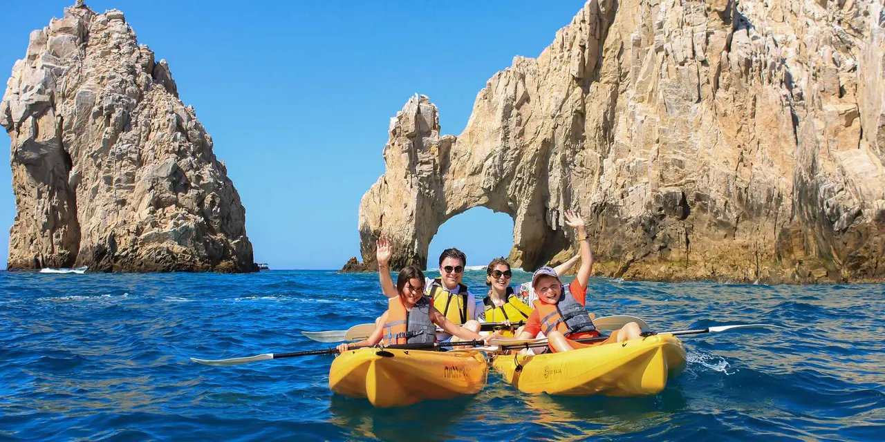Two yellow tandem kayaks with paddlers on blue water in front of the Arch of Cabo San Lucas