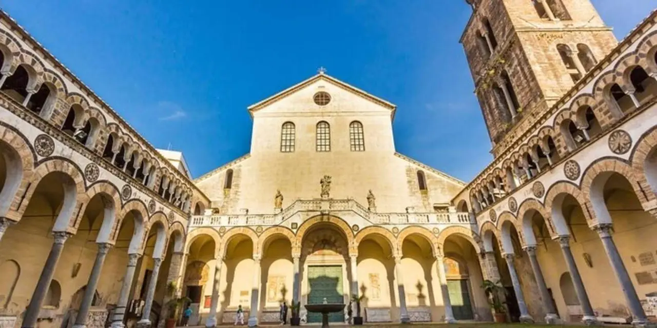 The arcaded courtyard and tall bell tower of Salerno Cathedral under a blue sky