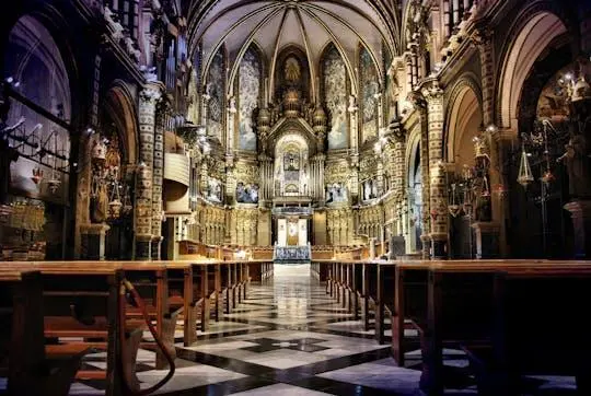 The ornate interior of the Montserrat basilica, with carved wooden pews in the foreground and a gilded altar glowing at the far end