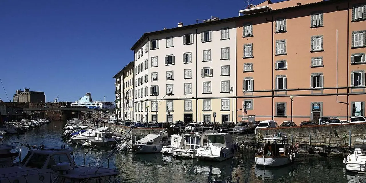 Tall pastel apartment buildings along a Livorno canal, with small boats moored below and a ship's superstructure at the far end