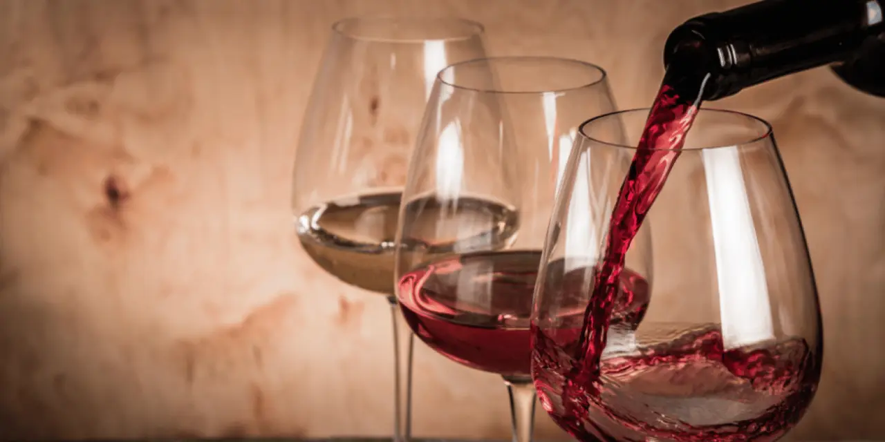 Red and rosé wine being poured into a row of glasses