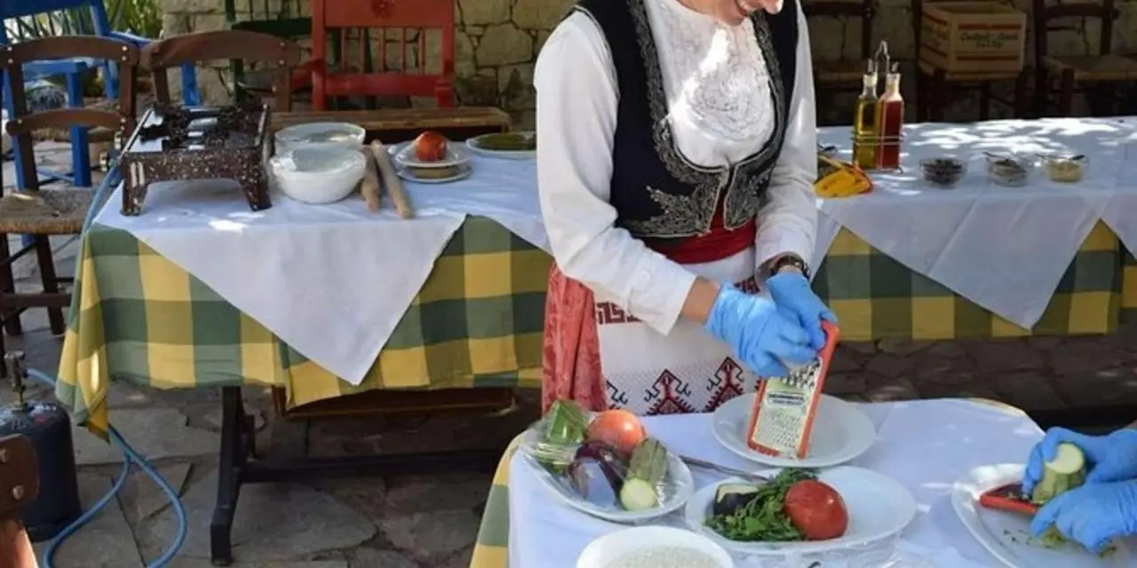 A host in traditional dress beside a table with a checked cloth in a stone courtyard