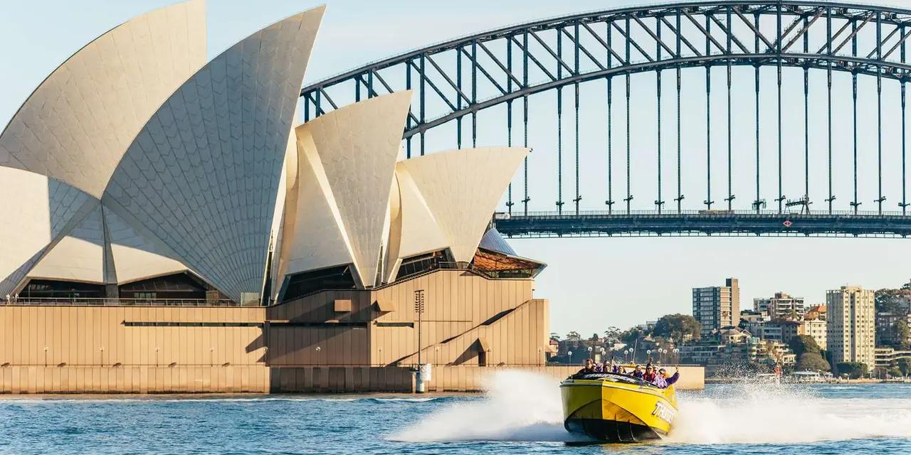 A yellow jet boat throwing up spray in front of the Opera House sails