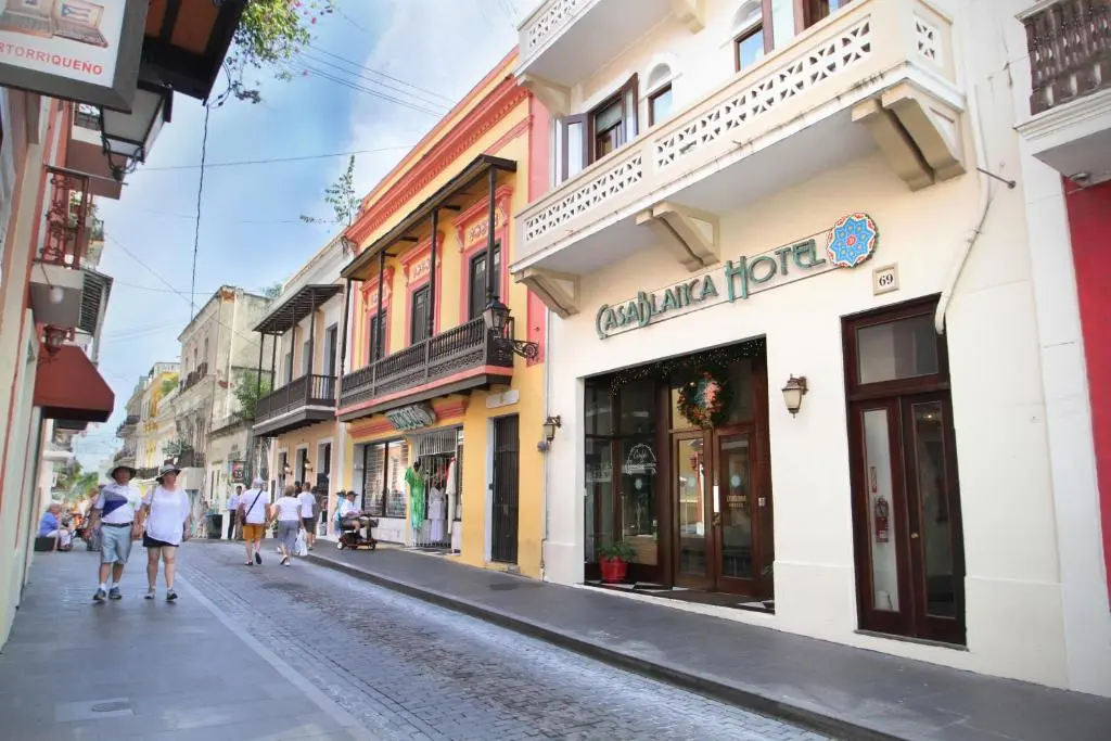 The CasaBlanca Hotel's white colonial front with balconies on a cobbled Old San Juan street, people walking past colourful buildings
