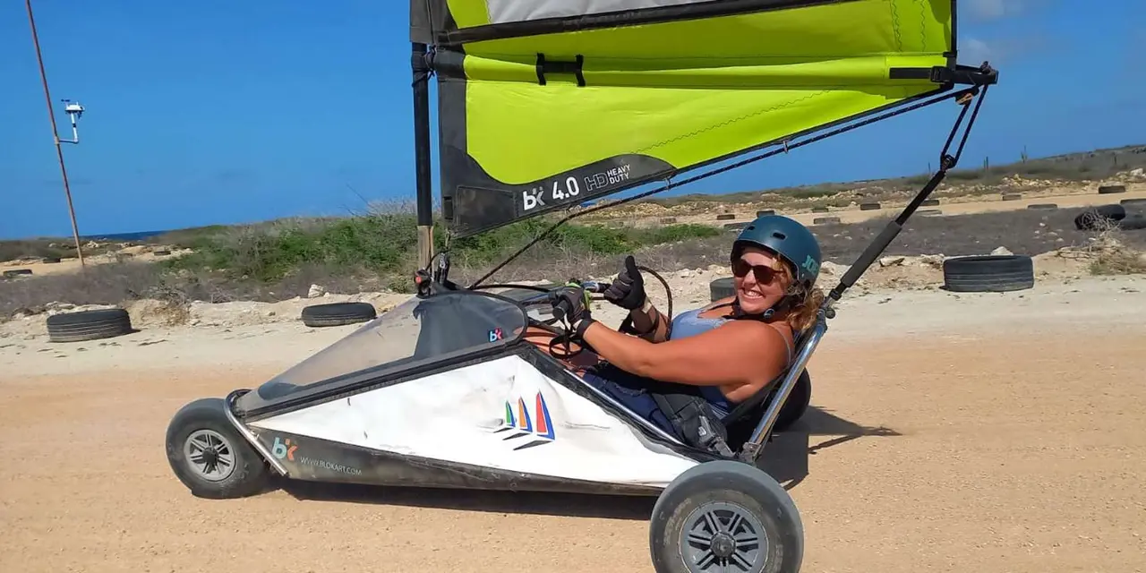 A smiling woman in a helmet sitting in a go-kart with a lime-green sail above her