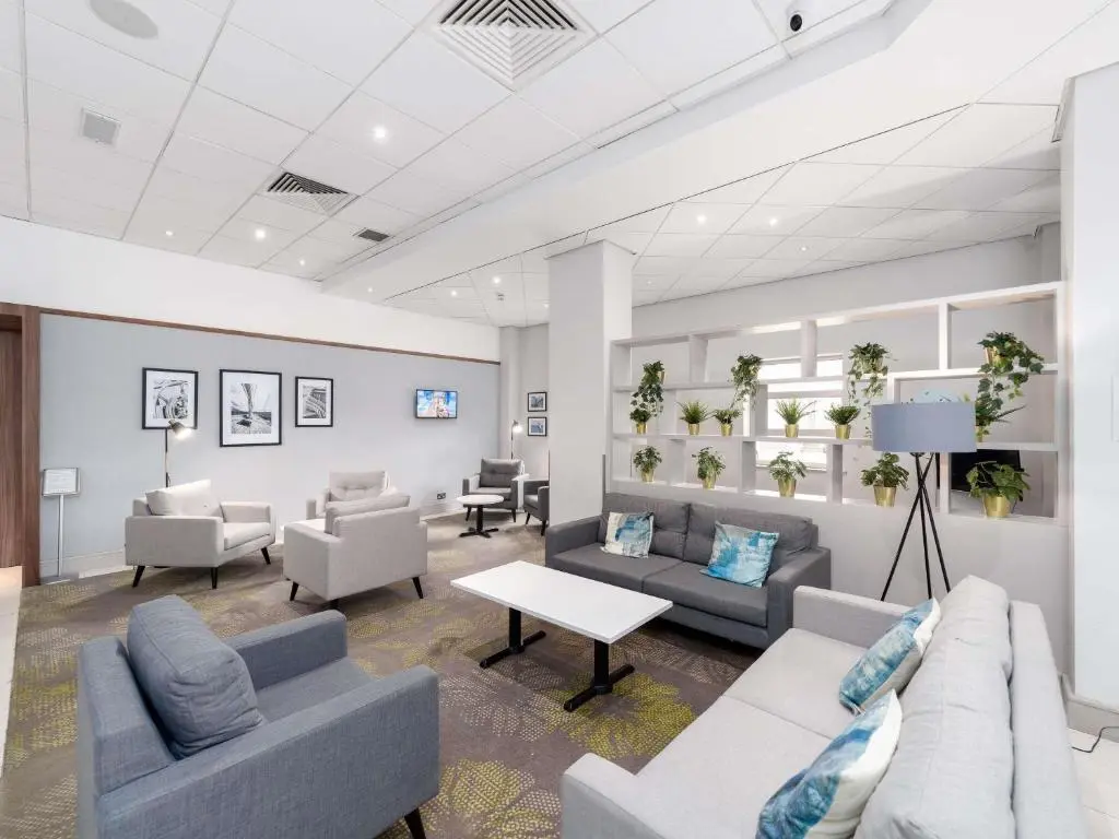 Novotel Southampton's lounge, with grey sofas and armchairs, a white coffee table, a shelf of potted plants and framed black-and-white prints
