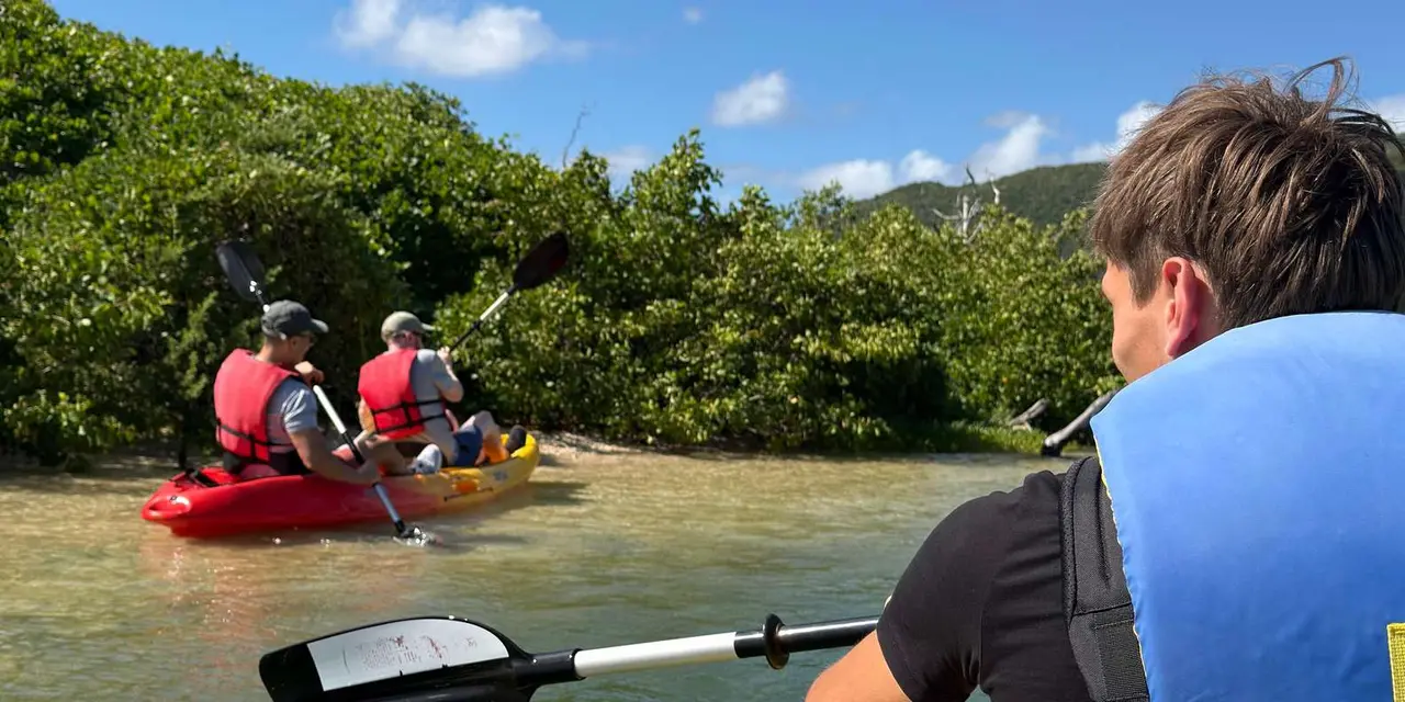 Kayakers in life jackets paddling a calm lagoon below wooded green hills