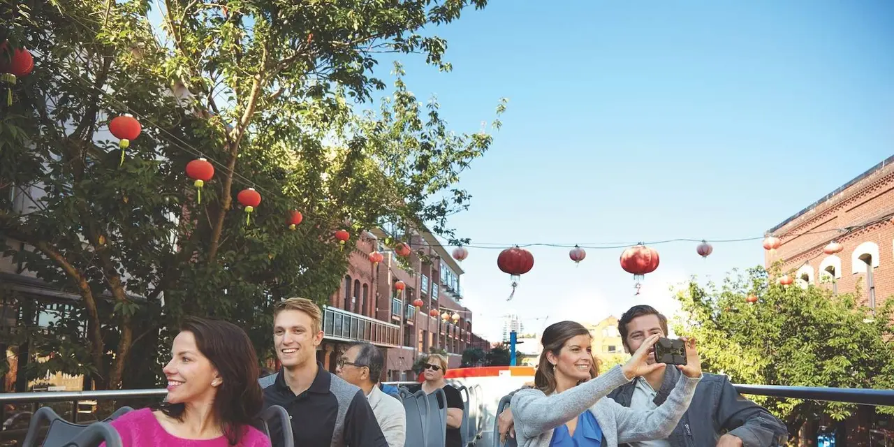 Passengers taking photos from the open top deck of a red bus in Chinatown under red lanterns