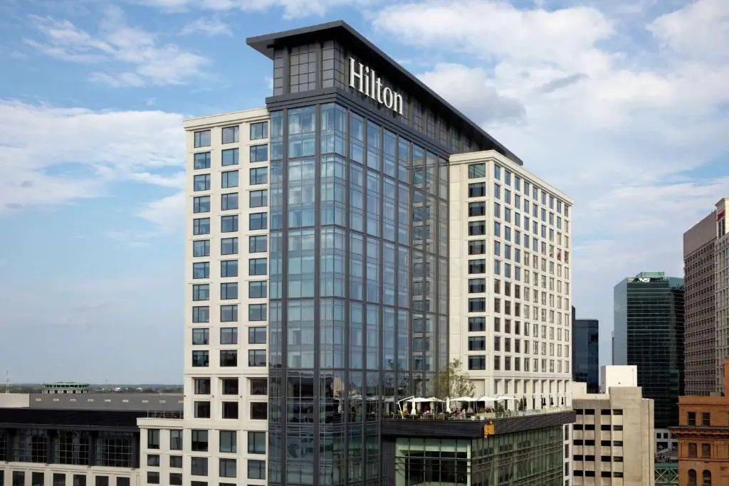 The glass-fronted Hilton Norfolk The Main tower against a blue sky, with its rooftop terrace and downtown Norfolk buildings around it