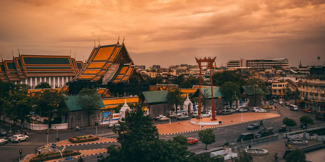Bangkok temple roofs and a tall red gateway under an orange evening sky