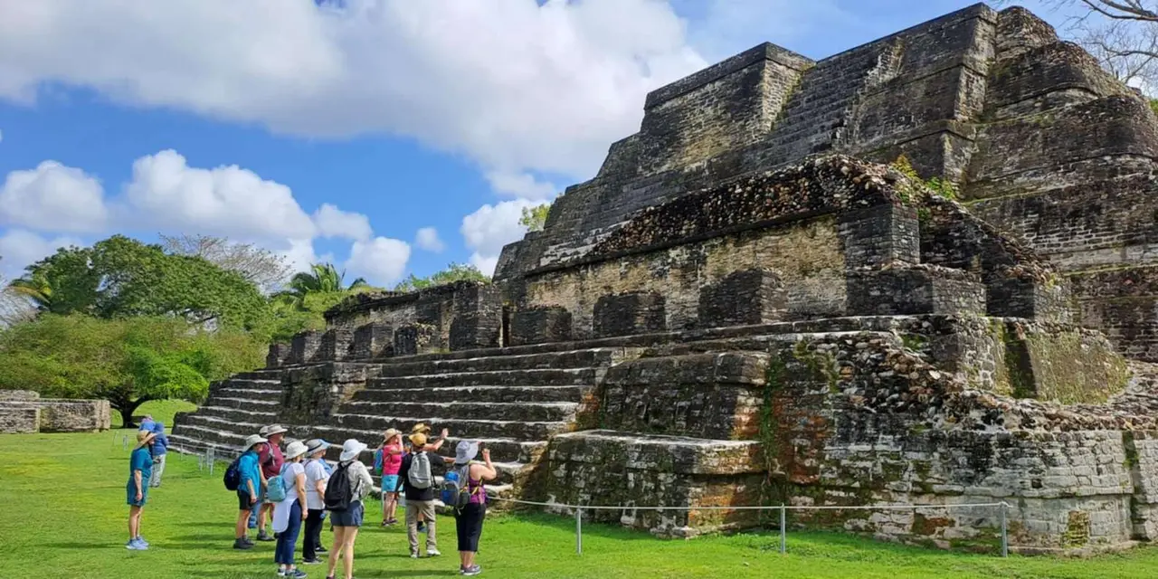 A group of visitors at the foot of a stepped stone Maya temple under a blue sky